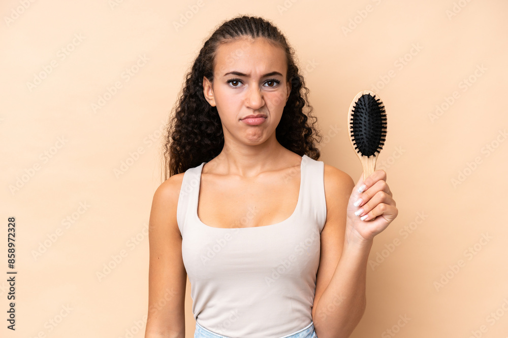 Young hispanic woman with hair comb isolated on beige background with sad expression Young hispanic woman with hair comb isolated on beige background with sad expression