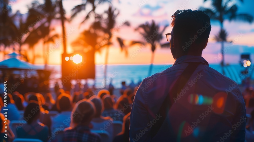 Silhouetted Man Gazing at Sunset Over a Crowd - A man in a blue shirt stands with his back to the camera, looking out at a sunset over the ocean. A crowd of people are gathered in front of him Silhouetted Man Gazing at Sunset Over a Crowd - A man in a blue shirt stands with his back to the camera, looking out at a sunset over the ocean. A crowd of people are gathered in front of him