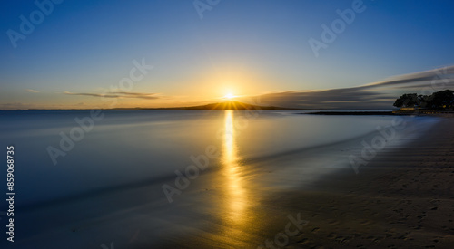 Obraz na płótnie Long exposure image of sunrise over the crest of Rangitoto Island. Milford Beach. Auckland. w salonie
