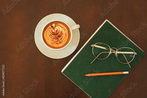 Beautiful hot latte, glasses, pencil and note book on wood table background with morning light.
