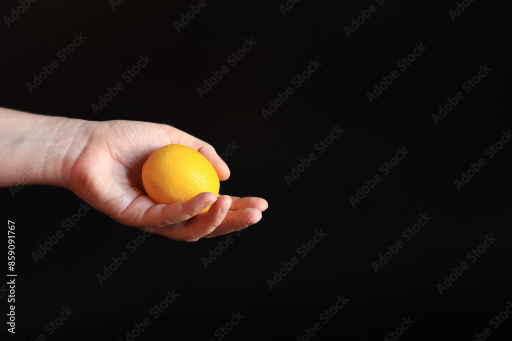 Close-up of a woman's hand holding a ripe lemon. Yellow lemon in hand on a black background. Ingredient. Fruit and food concept. Citrus Close-up of a woman's hand holding a ripe lemon. Yellow lemon in hand on a black background. Ingredient. Fruit and food concept. Citrus