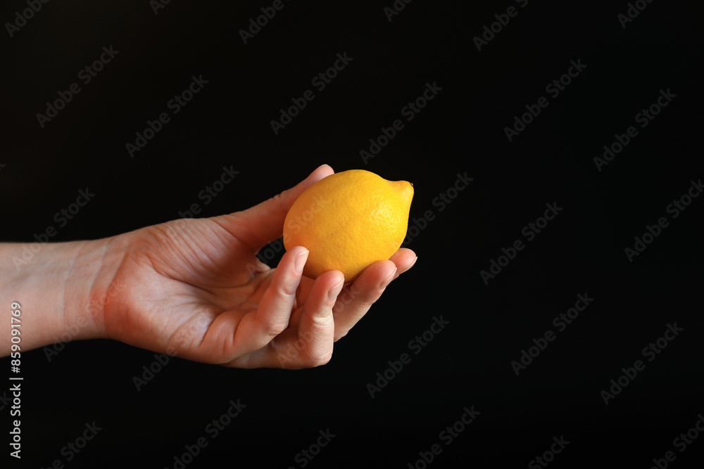 Close-up of a woman's hand holding a ripe lemon. Yellow lemon in hand on a black background. Ingredient. Fruit and food concept. Citrus Close-up of a woman's hand holding a ripe lemon. Yellow lemon in hand on a black background. Ingredient. Fruit and food concept. Citrus