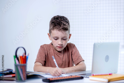 Cute pupil boy studying at home writing in exercise book doing homework, learning at home table