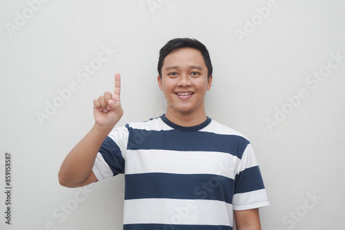 Young Asian man with striped t shirt showing one finger sign isolated on white. Male gesturing number one sign photo