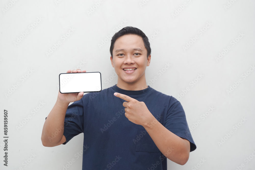 Young Asian man smiling and pointing to smartphone screen isolated on white background. lifestyle and advertising concept. Men using blue shirt holding phone mockup Young Asian man smiling and pointing to smartphone screen isolated on white background. lifestyle and advertising concept. Men using blue shirt holding phone mockup