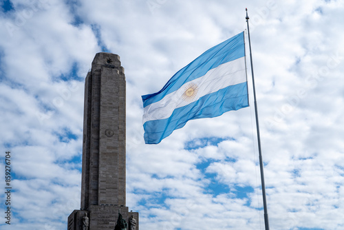 Bandera Argentina izada en altura y flameando al viento con el Monumento Nacional a la bandera de fondo photo