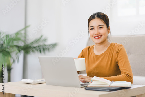 Smiling Asian Businesswoman Working on Laptop with Coffee at Home.