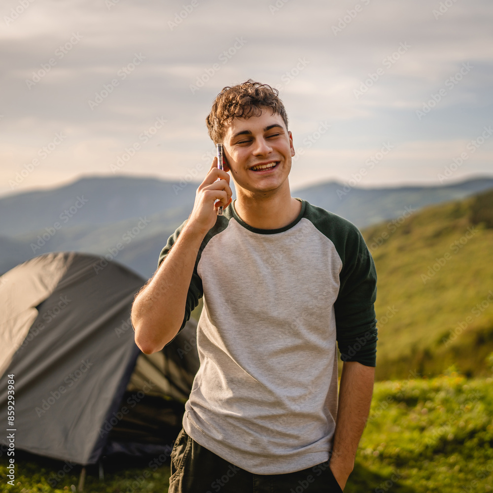 Young boy stand in front tent and talk on mobile phone on the mountain Young boy stand in front tent and talk on mobile phone on the mountain
