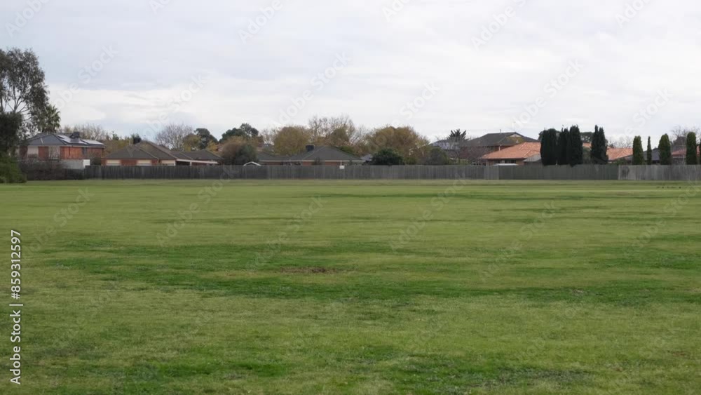 A row of residential houses near a large open green space in a public park. Parkland in the neighborhood for recreational and sports use. Cambridge reserve, Hoppers Crossing Melbourne Australia.