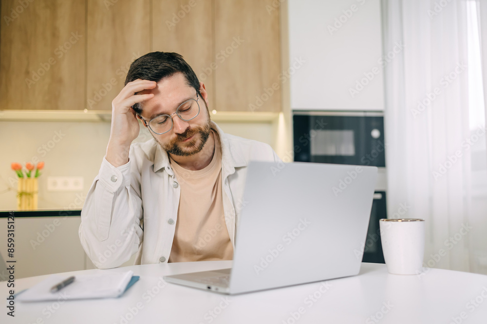 Bad news, lack of understanding of new app, info overload, device malware concept. Young man in glasses sit at table touch forehead feels confused. Remote work Bad news, lack of understanding of new app, info overload, device malware concept. Young man in glasses sit at table touch forehead feels confused. Remote work