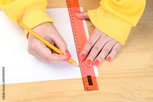 Women's hands draw lines on paper using a ruler and pencil.