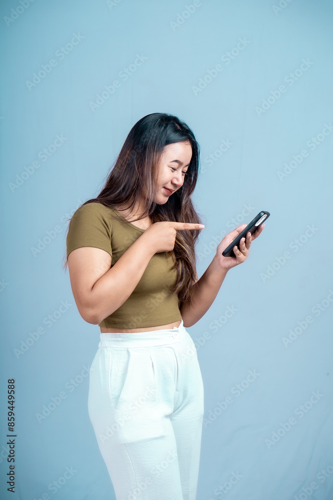 A young Asian woman with an expression holding a smartphone isolated on a blue background A young Asian woman with an expression holding a smartphone isolated on a blue background