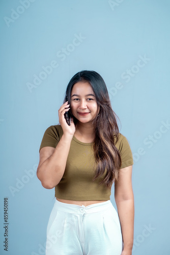 A young Asian woman with an expression holding a smartphone isolated on a blue background