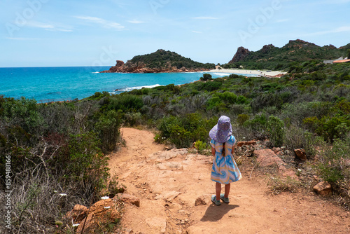 Little girl in dress standing on the path to wild hidden Su Sirboni beach and red rock formations in province of Nuoro on Sardinia (Sardegna) island in Italy. Tyrrhenian Sea. © Sofiia.Popovych