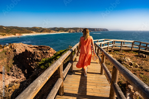 Beautiful woman walking on cliff to sunny beach Portugal, Algarve, Amado praia