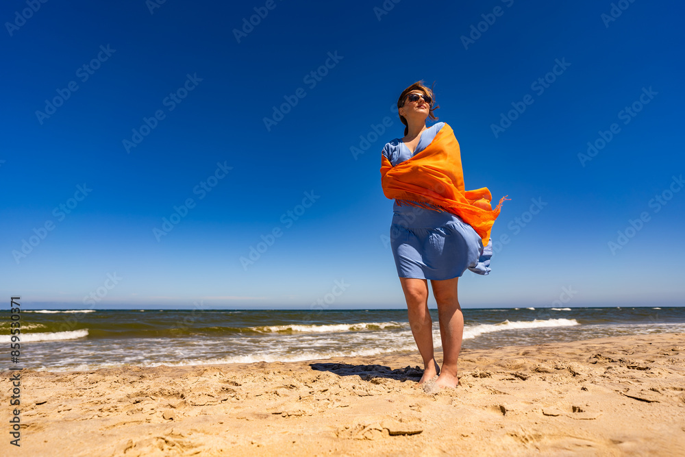 Beautiful woman holding shawl walking on sunny beach Beautiful woman holding shawl walking on sunny beach