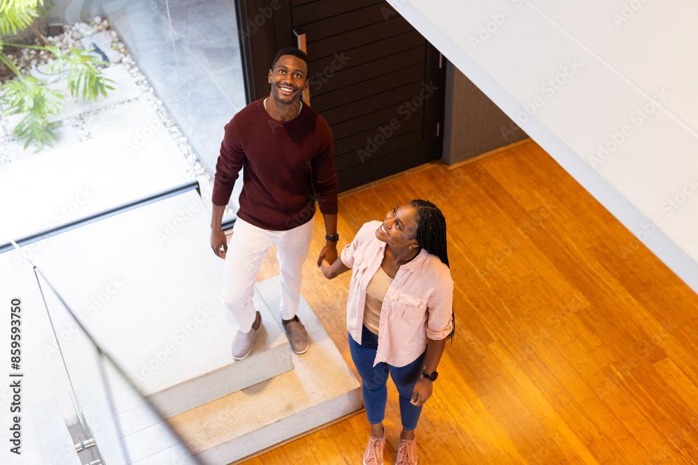 Holding hands, smiling, young couple standing on stairs in modern home Holding hands, smiling, young couple standing on stairs in modern home