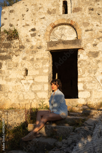 Young beautiful woman is sitting in front of old building. Ancient city, history, fashion, tourist and tourism concept photo.