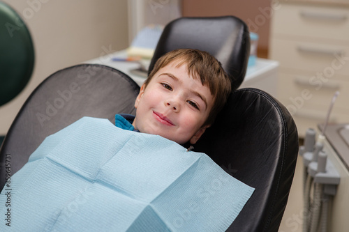 A cute little boy in a dental chair treats his teeth, smiling and happy