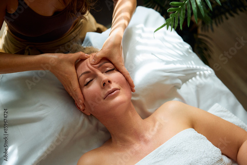 Obraz na plátně Mature woman having face massage by masseuse in a spa