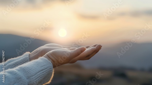A serene scene of hands extended towards a glowing sunset over a blurred mountain landscape, capturing a peaceful and reflective moment. photo