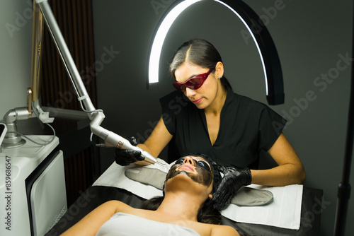Latin woman undergoing a YAG laser treatment for skin rejuvenation and beautification at a well-equipped aesthetic clinic photo