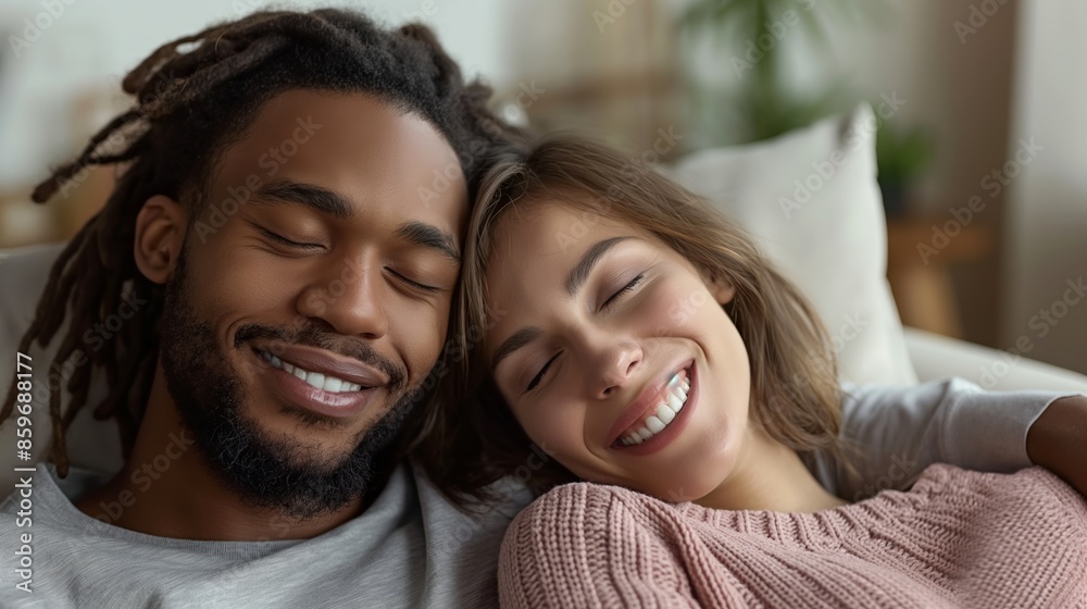 A young man with dreadlocks and a woman in a pink sweater are sitting on a couch and laughing indoors