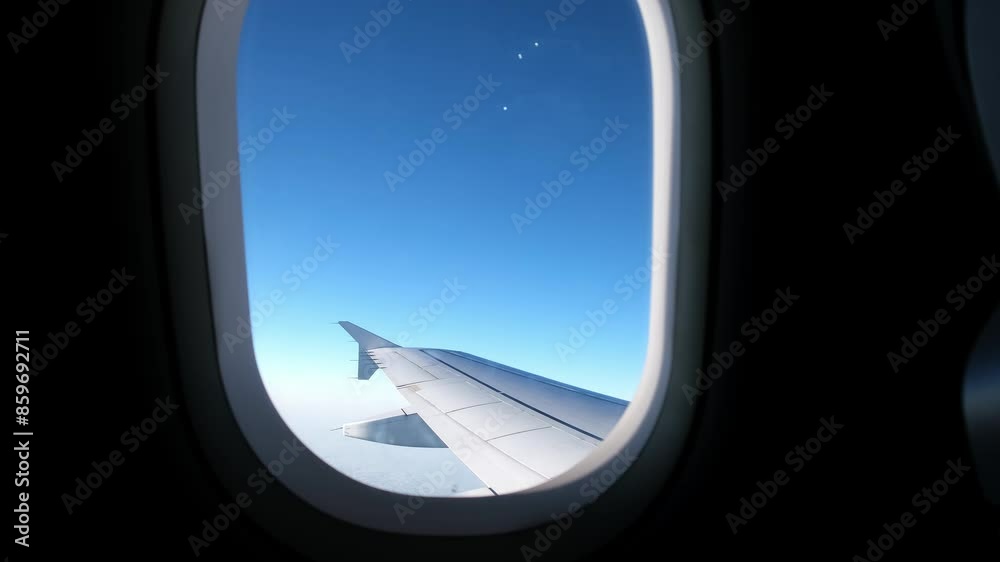 View of an airplane wing from a porthole against a blue sky background. A passenger plane flies above the clouds in the morning light. The concept of traveling by air. Fear of heights, aerophobia. 4K View of an airplane wing from a porthole against a blue sky background. A passenger plane flies above the clouds in the morning light. The concept of traveling by air. Fear of heights, aerophobia. 4K