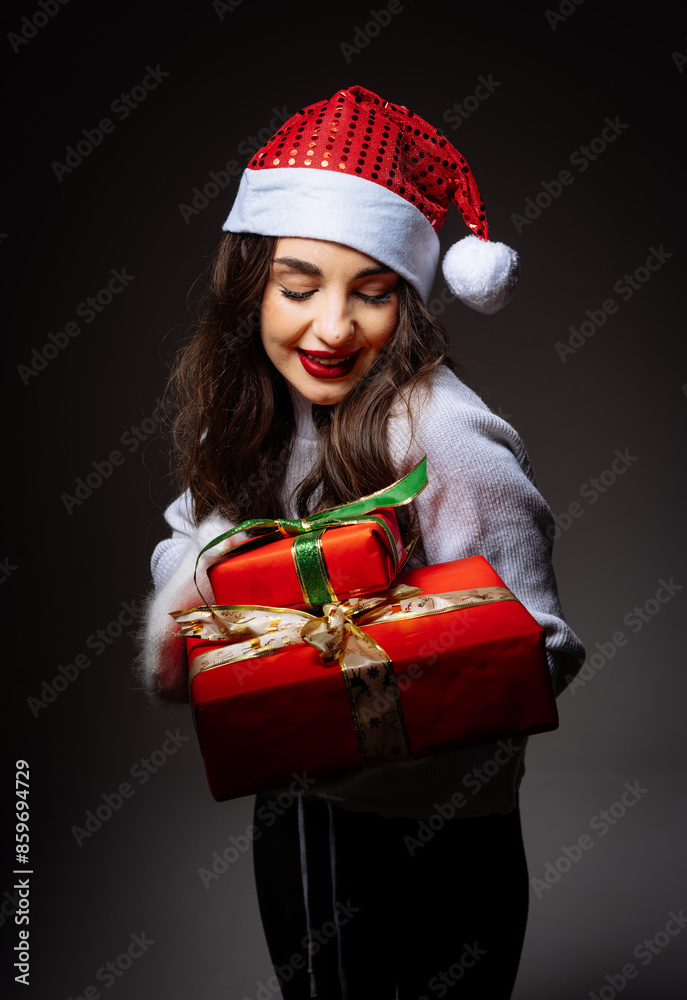 Woman Holding Christmas Gifts. A woman in a Santa hat holds two Christmas presents wrapped in red paper and decorated with green and gold ribbons. Woman Holding Christmas Gifts. A woman in a Santa hat holds two Christmas presents wrapped in red paper and decorated with green and gold ribbons.