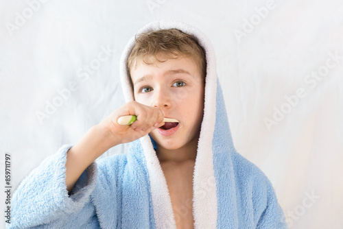 small child, boy in a blue terry robe with a toothbrush on white. A child brushes his teeth. Healthcare and dental care