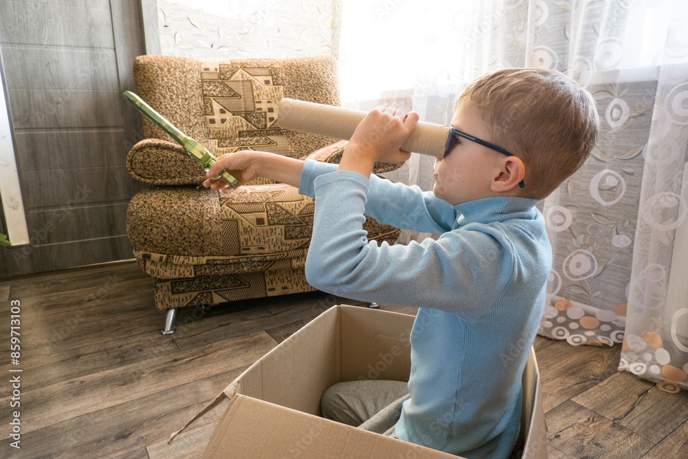 Playful cheerful child, boy looking into a cardboard tube, sitting in a box