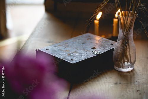 Old Bible with Cross Lock in Rustic Scene with Wooden Bench with Rye and Candles Burning for Christian Studies and Scripture Reading, Purple Flower Foreground and Soft Light photo