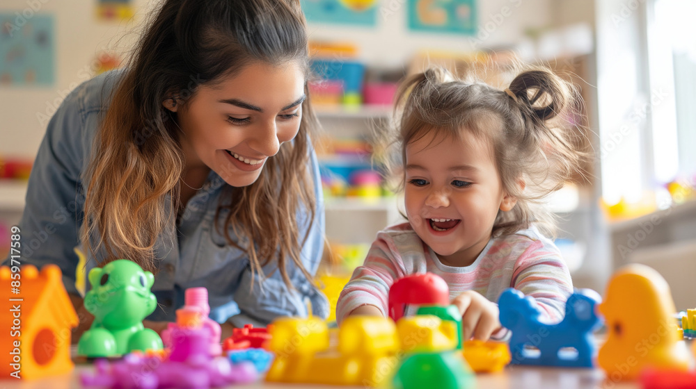Fototapeta premium smiling female teacher and preschool child playing together with colorful toys at kindergarten