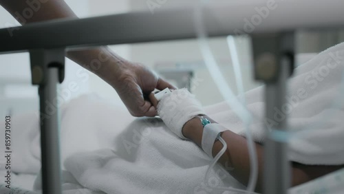 Close up shot of mother holding hand of sick daughter while lying down on bed in the hospital