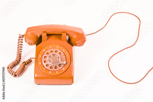Vintage orange rotary dial telephone with a coiled cord, on a white background, studio shot.