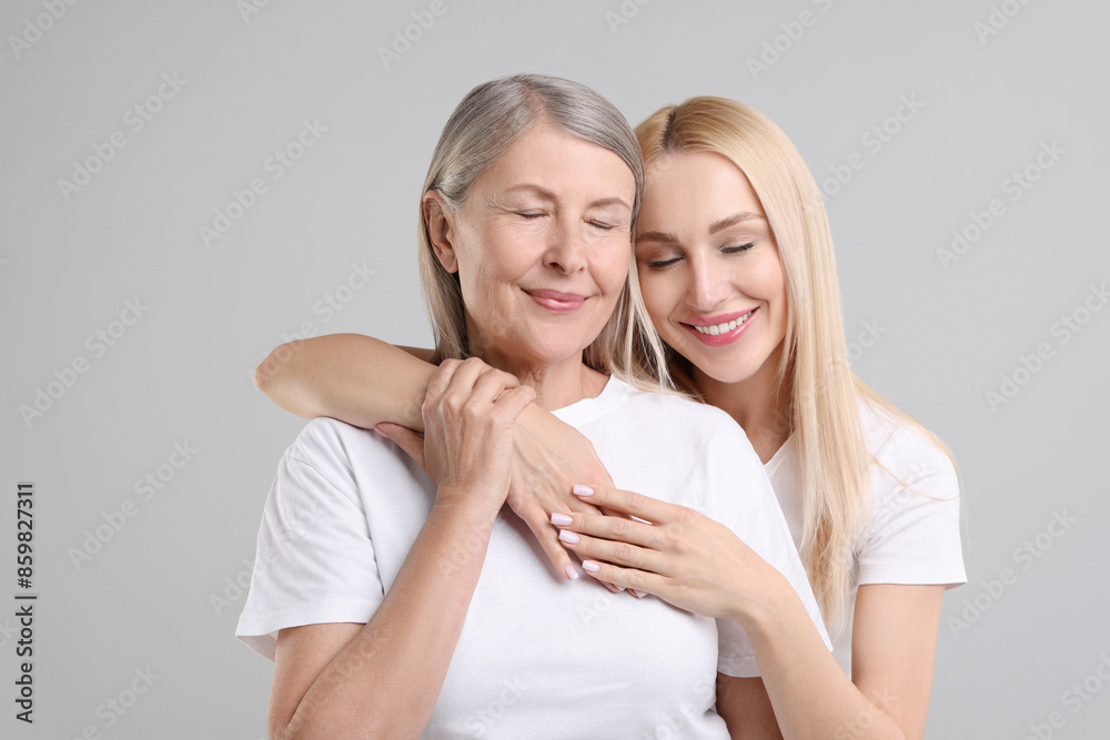 Family portrait of young woman and her mother on light grey background Family portrait of young woman and her mother on light grey background