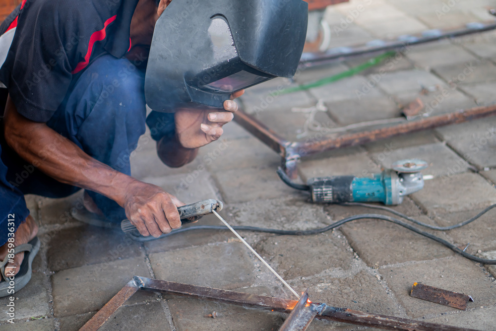 Man welding metal pieces on a paved surface Man welding metal pieces on a paved surface