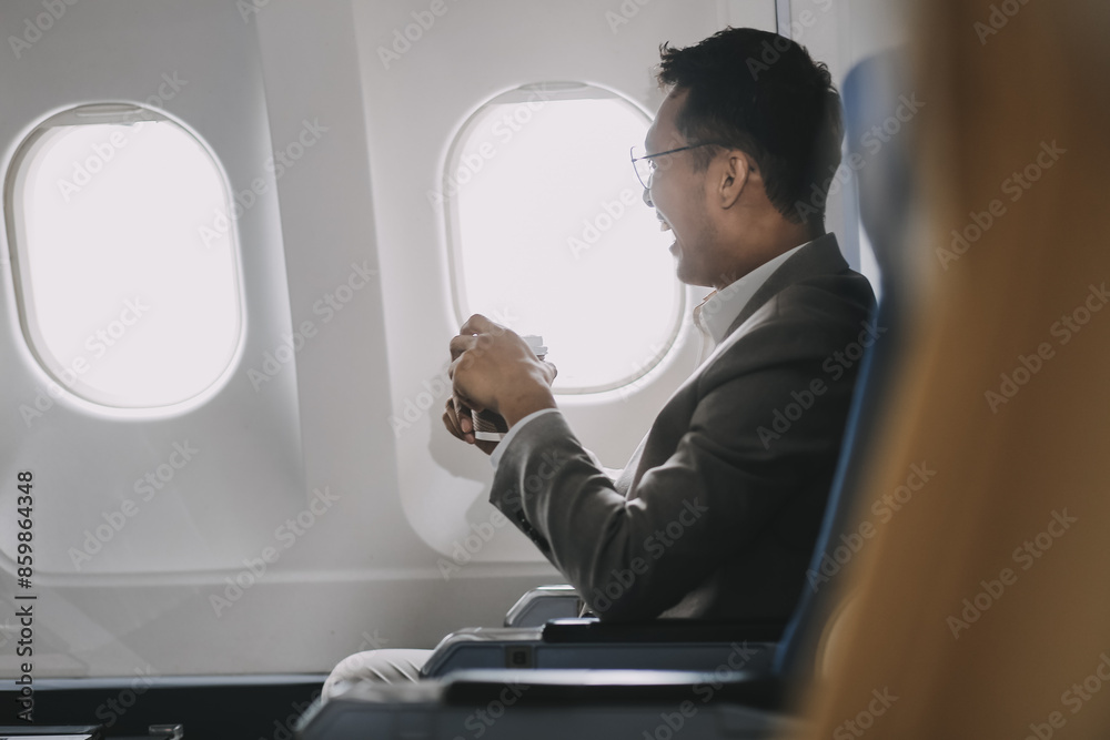 Asian businessman enjoying enjoys a coffee comfortable flight while sitting in the airplane cabin, Passengers near the window. Asian businessman enjoying enjoys a coffee comfortable flight while sitting in the airplane cabin, Passengers near the window.