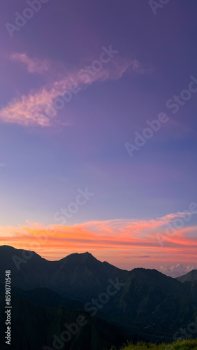 A tranquil sunset at Bukit Anak Dara Sembalun, Lombok, with pastel colors of pink and orange in the sky, highlighting the silhouette of the mountains and creating a serene atmosphere. 