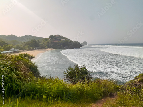 Harmony of Elements: Ngandong Beach's Serenade - Waves Gently Caress the Shore as Verdant Grass Whispers in the Coastal Breeze photo