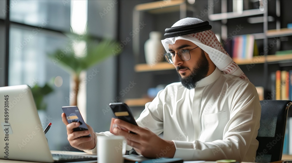 A man in an arabic headdress using his phone and laptop. A man in an arabic headdress using his phone and laptop.