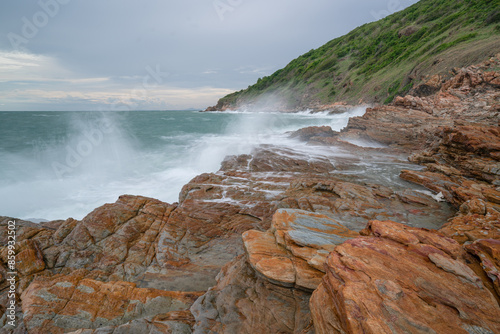 Waves crash against a rocky shoreline with mountains in the background