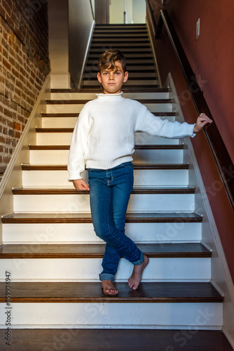 Barefoot boy in blue jeans and white sweater standing casually on stairs