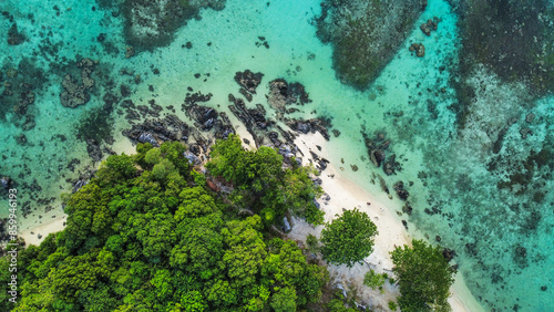 An aerial view of the lush green forest meeting the clear turquoise waters at Karimun Jawa, Indonesia, featuring rocky formations and a pristine beach, highlighting the natural beauty of this tropical photo