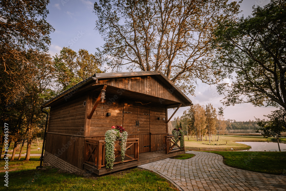 Blome, Latvia - September 11, 2023 - A charming wooden cabin with flower-adorned porches, set in a scenic landscape with trees, a pond, and a winding stone pathway. Copy space... Blome, Latvia - September 11, 2023 - A charming wooden cabin with flower-adorned porches, set in a scenic landscape with trees, a pond, and a winding stone pathway. Copy space...