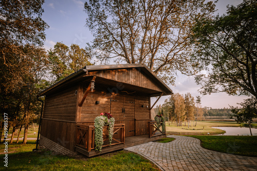 Blome, Latvia - September 11, 2023 - A charming wooden cabin with flower-adorned porches, set in a scenic landscape with trees, a pond, and a winding stone pathway. Copy space... photo