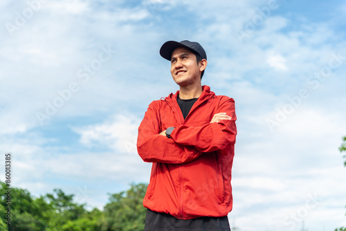 Portrait of a smiling young adult asian man wearing sportswear in running track. Happy handsome male standing with arms crossed outdoors. Head shot. Athlete after a morning run. © BJ Day Stock
