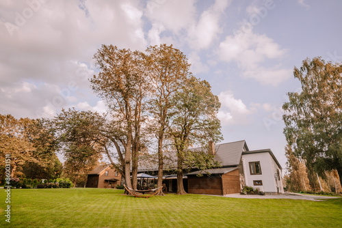 Blome, Latvia - September 11, 2023 - Spacious yard with a hammock and trees, adjacent to a modern house, under a blue sky with clouds, creating a serene and inviting atmosphere. Copy space. photo