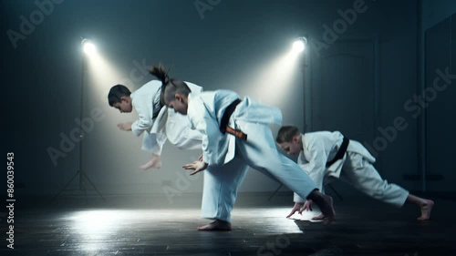 Three concentrated boys training karate at smoky background. Group of young karate practitioners in white kimono, perform synchronized martial arts katas. Practicing karate moves at class indoors photo