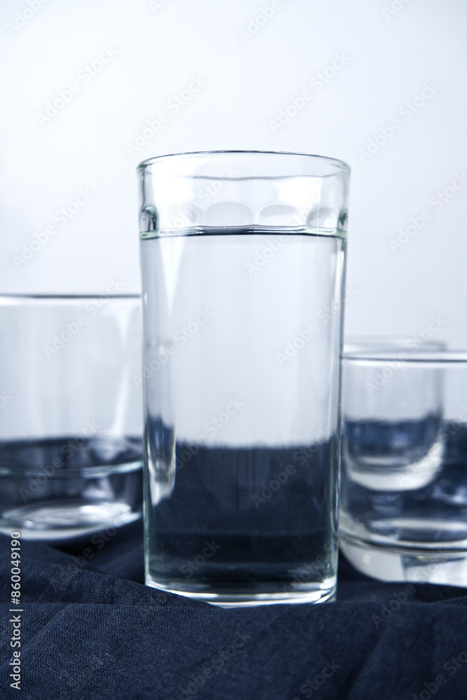 Glass of water with white background. Drinking, clean water, healthy drink, liquid, and tableware concepts. Vertical image of pure and room temperature of water glasses on black fabric. Glass of water with white background. Drinking, clean water, healthy drink, liquid, and tableware concepts. Vertical image of pure and room temperature of water glasses on black fabric.